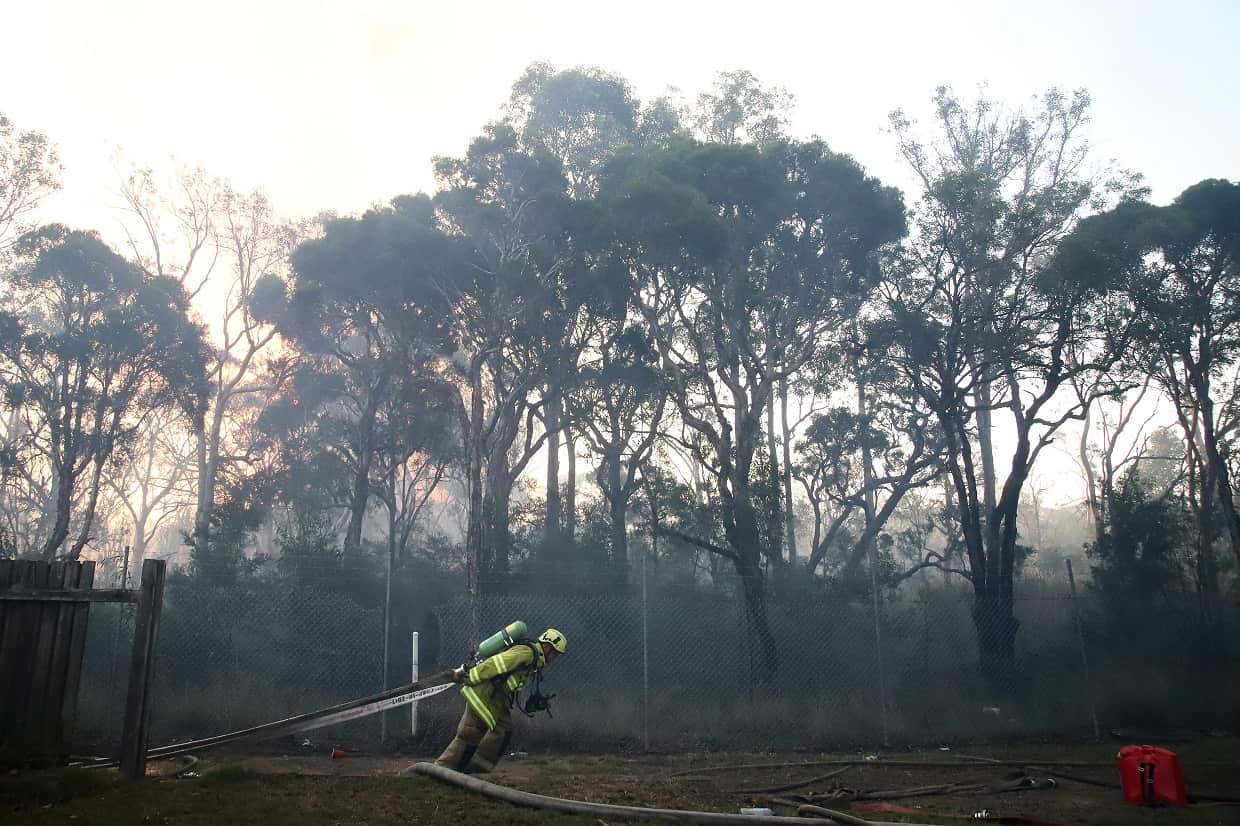 A firefighter pulls a hose as an out-of-control grass fire burns at Holsworthy in Sydney, Saturday, April 14, 2018. (AAP Image/Jeremy Ng) NO ARCHIVING