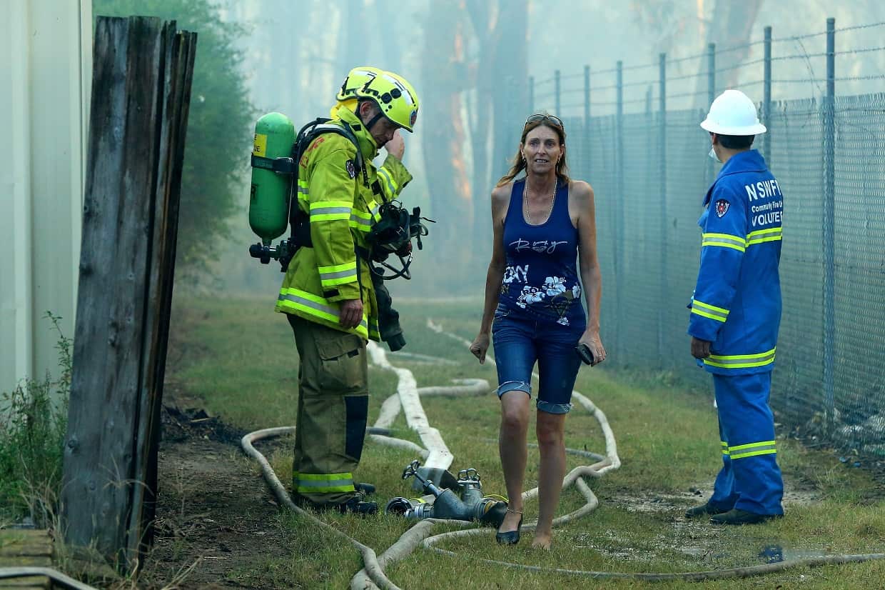 A local resident walks past firefighters as the fire burns at Holsworthy.