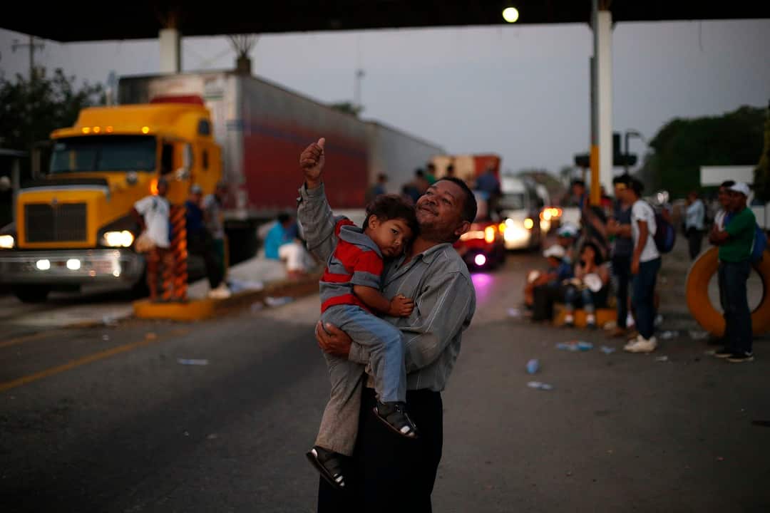A man holding his son tries to flag down a passing truck for a free ride, as the migrant caravan moves north.