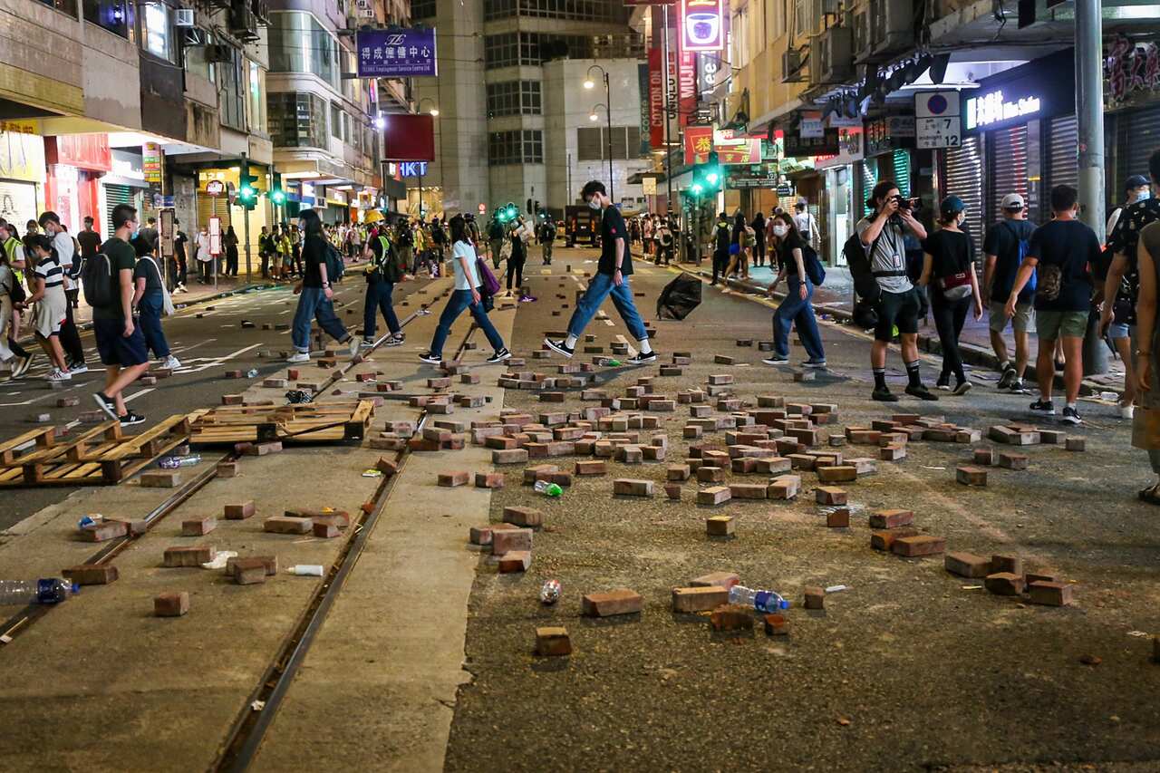 Passersby walk past bricks that have been dug up and laid out on the street as a way to slow down police during demonstrations.