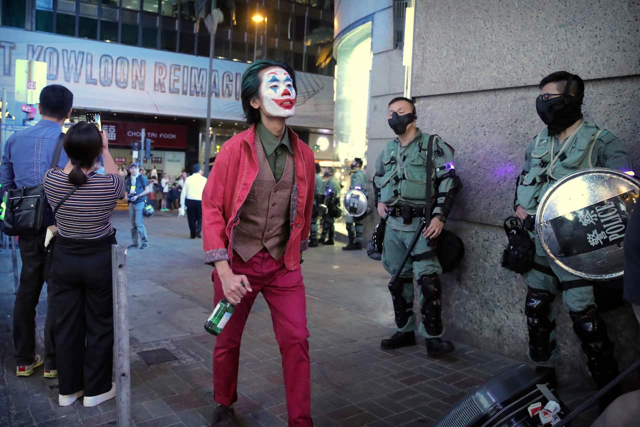 A man in a Halloween costume walks past police officers in riot gear in Hong Kong.