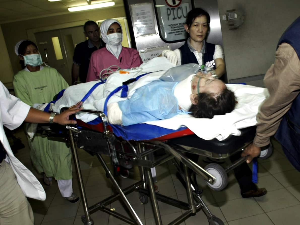 Cynthia Banham, center, one of the victims of Indonesia's jetliner fire, is taken by doctors and hospital staff as she leaves enroute for Melbourne.