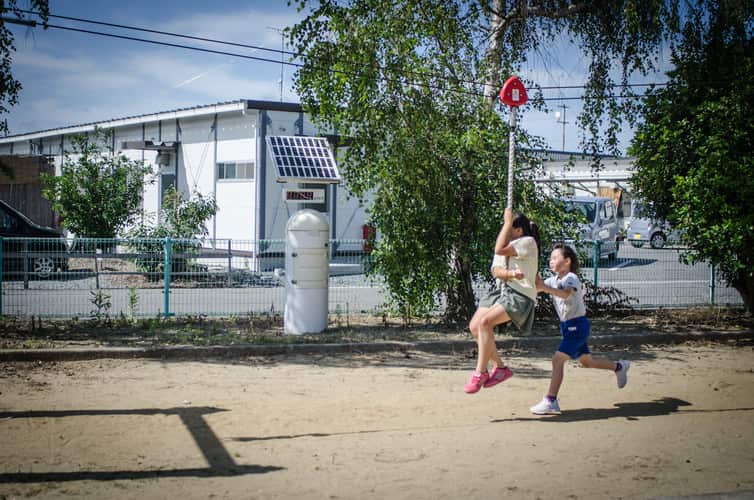Two girls play on a swing next to a radiation monitor and their temporary housing in Minamisōma, Fukushima prefecture.