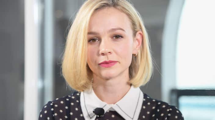 A woman with shoulder-length blonde hair, wearing a black polka dot top, looks on.