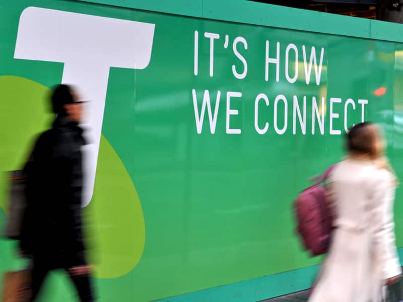 People walk past a Telstra sign.