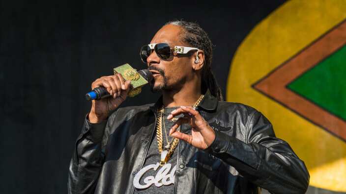 A man wearing a leather jacket and sunglasses singing into a microphone