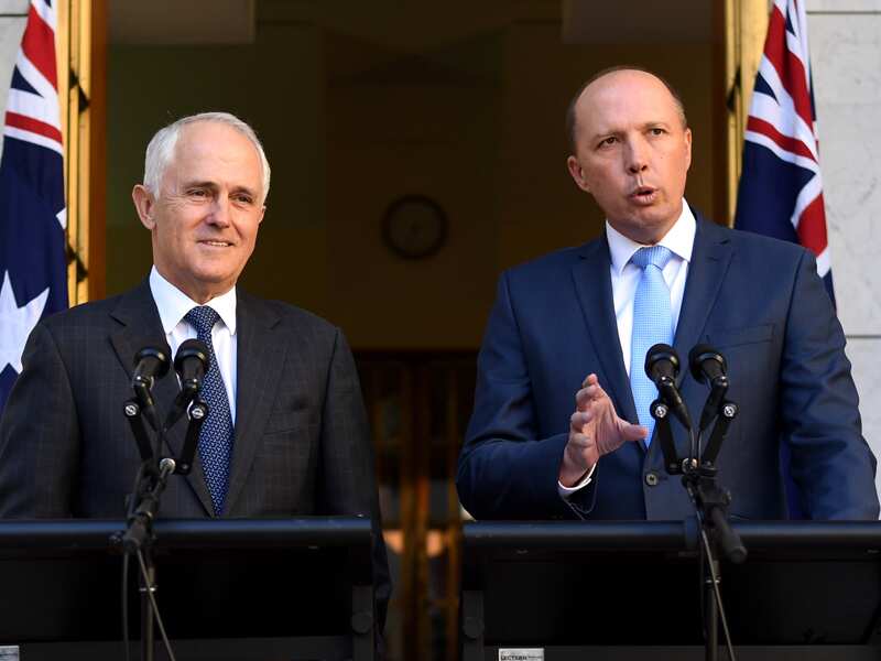 Two men in suits stand at lecterns.