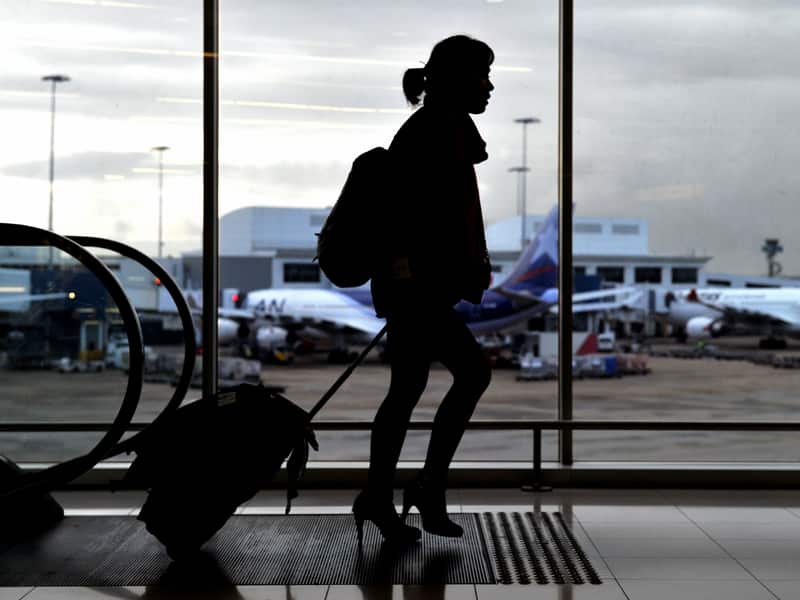 A woman pulling a suitcase on wheels is silhouetted against a window showing planes outside