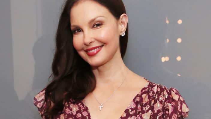A woman with long brown hair wearing a maroon-coloured dress smiles.
