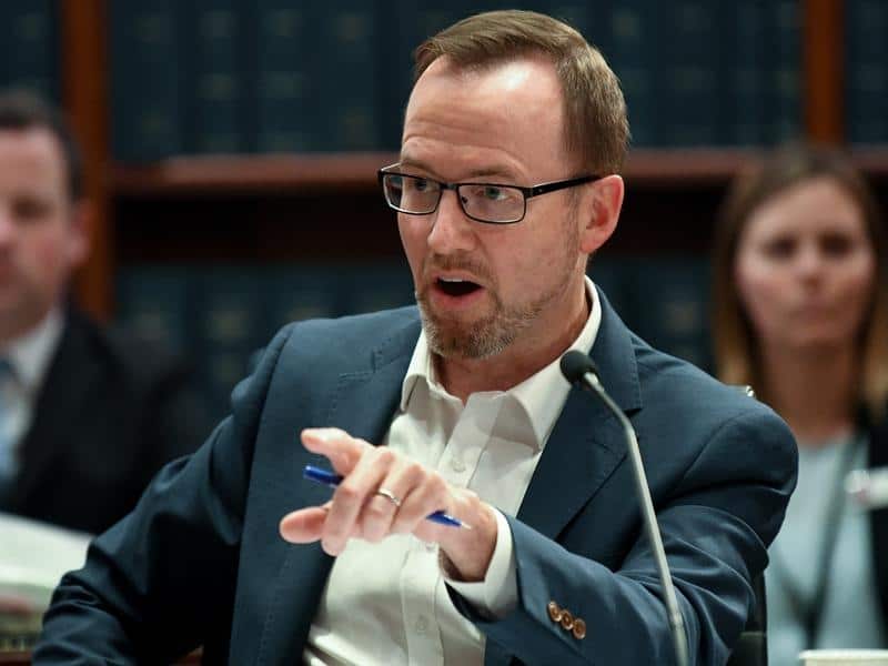 Man in glasses and suit jacket speaking into a microphone.