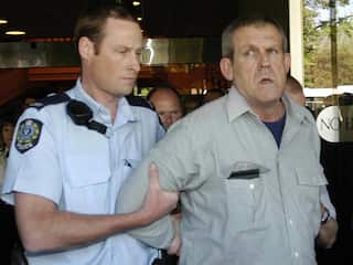 Bradley John Murdoch being walked on by a police officer in a blue uniform.