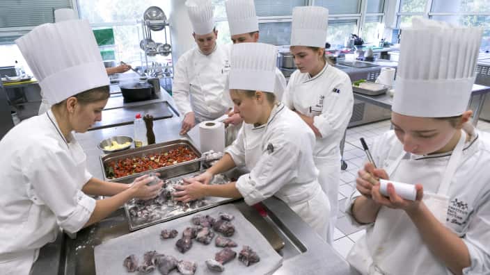 A group of young people handle food dressed in white uniforms