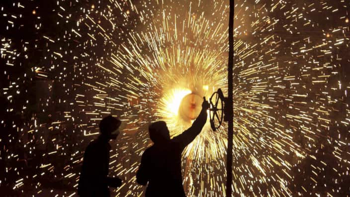 Two people stand before the glow of a firecracker, its sparks radiating in a circular pattern.