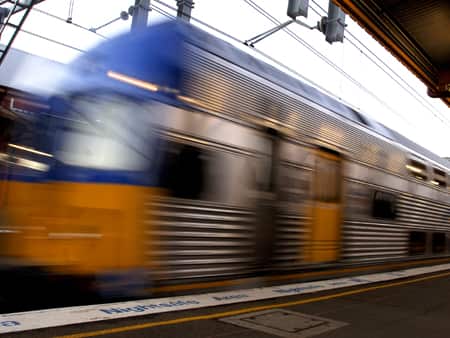 A blurry image of a silver train next to a platform and travelling fast