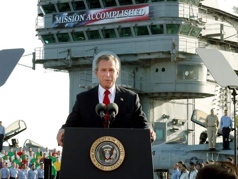 George W Bush stands at a lectern in front of a banner on a ship that says 'Mission accomplished'.