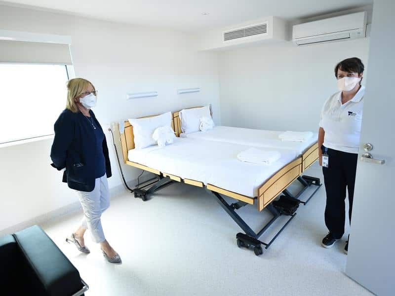 A woman and a man in a room. A bed is in the corner.