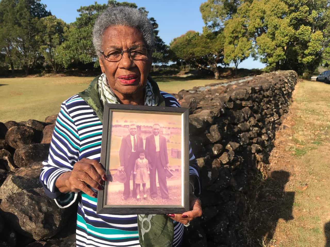 Aunty Lill Engstrom carries a photo of her father by the wall he build about 120 years ago. 