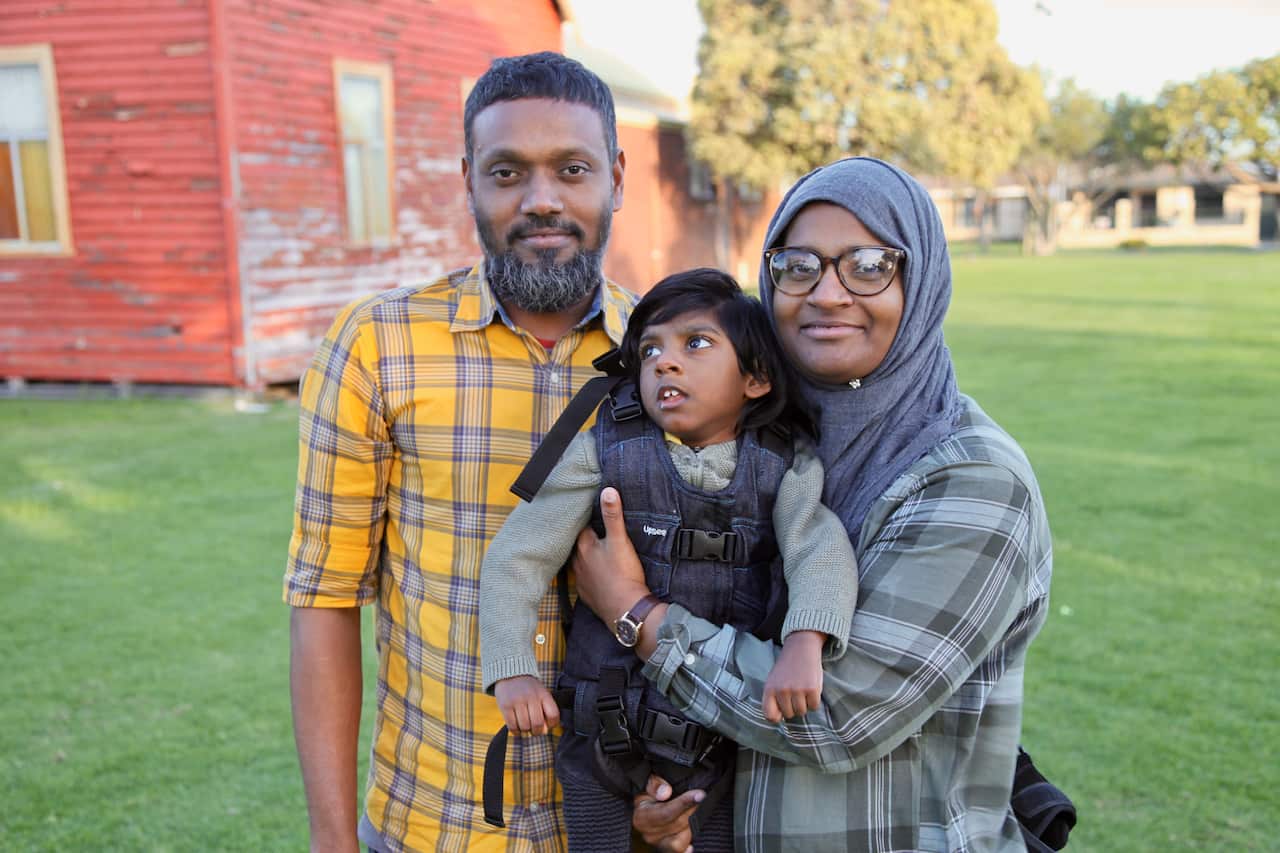 A father and mother standing outside holding their son.