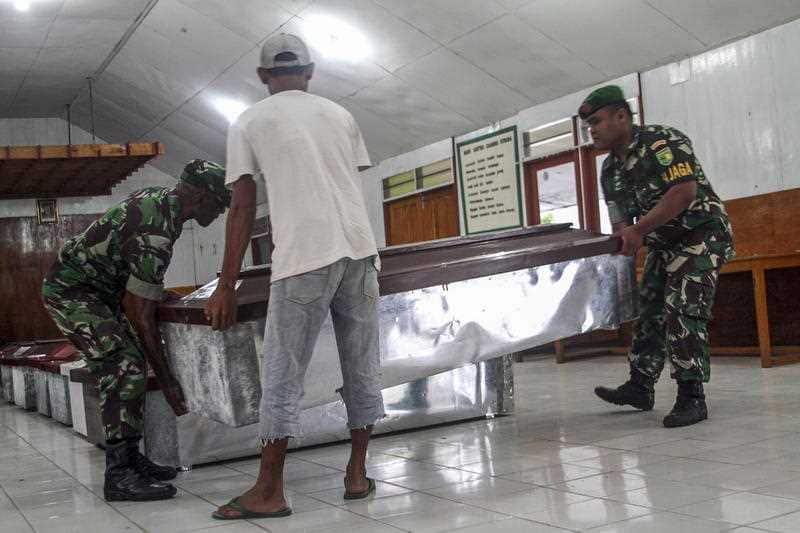 Indonesian troops and workers prepare coffins for the slain construction workers.