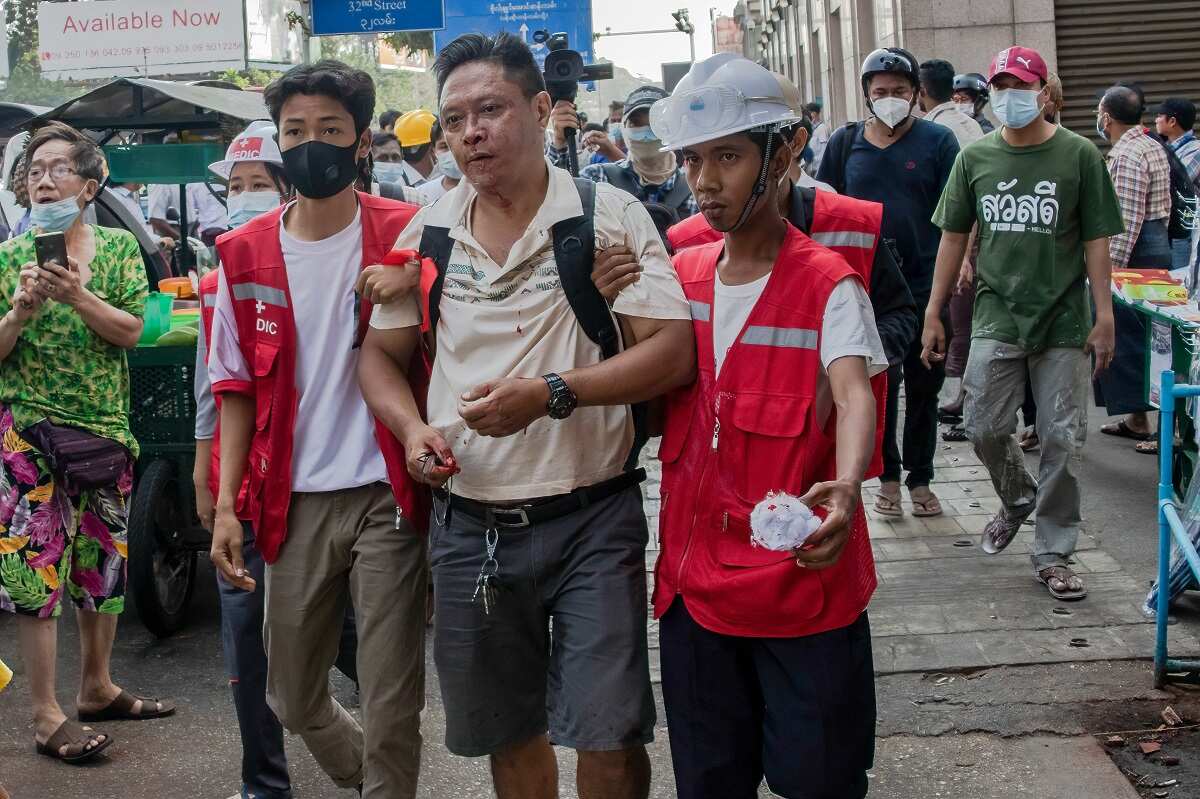 An anti-coup protester is seen covered in blood and helped by two young men after he was assaulted by military supporters during the rally.