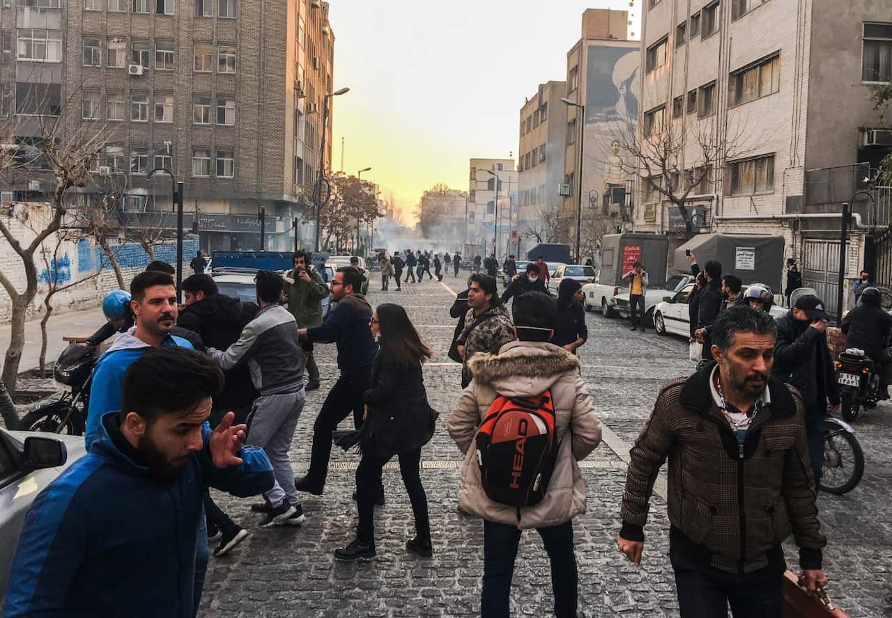 People are affected by tear gas fired by anti-riot Iranian police to disperse demonstrators in a protest over Iran's weak economy, in Tehran (AAP)