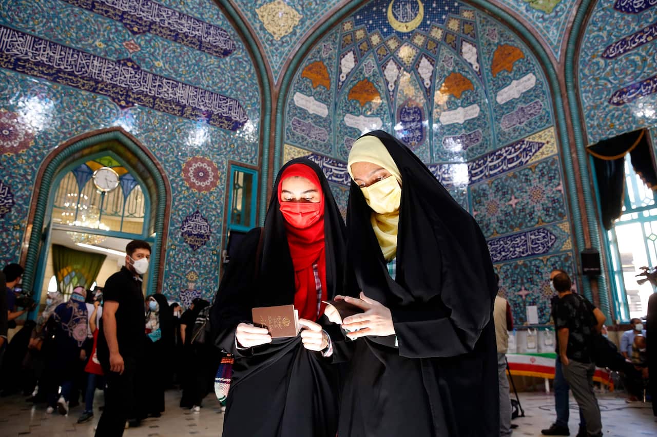 Two Iranian women check their ID papers to cast their votes at a polling station during the presidential election in Tehran, Iran.