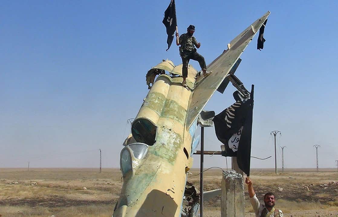 A person holding a flag who is standing on the wing of a destroyed fighter jet.