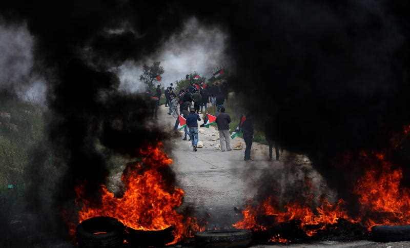Palestinian protesters seek cover from tear gas during clashes with Israeli forces in the West Bank region.