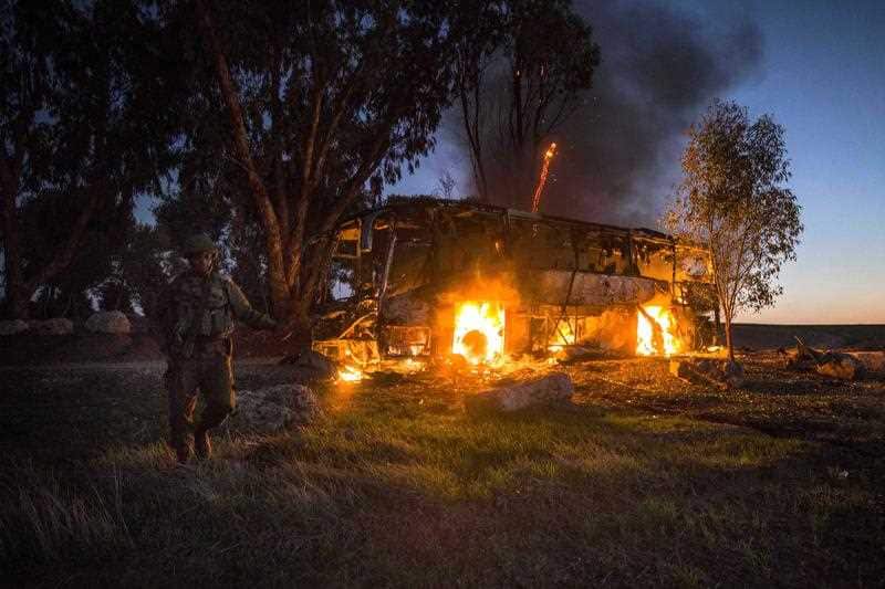 An Israeli soldier stands near a burning bus after it was hit by a mortar shell fired from Gaza near the Israel Gaza border.