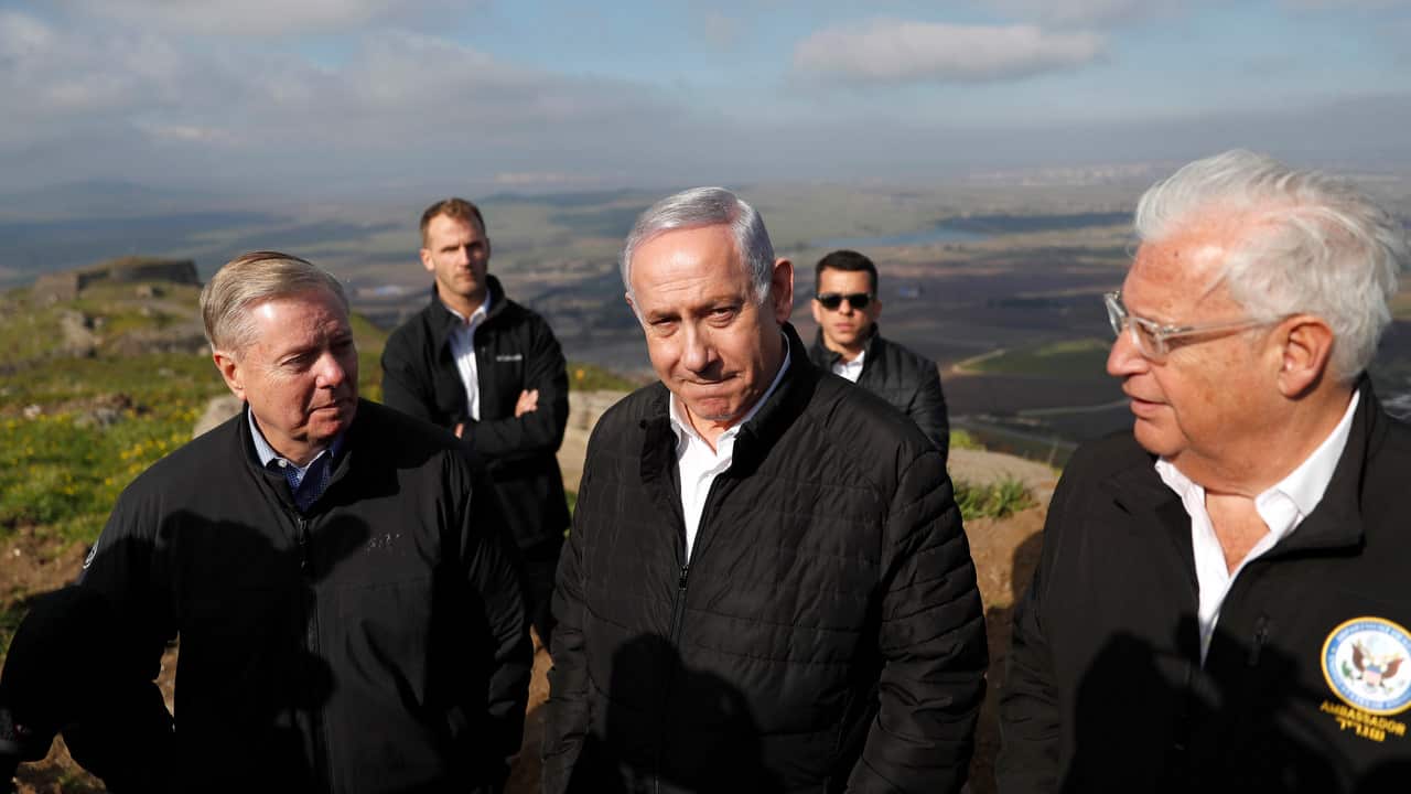 Five men stand on a hill in black jackets.