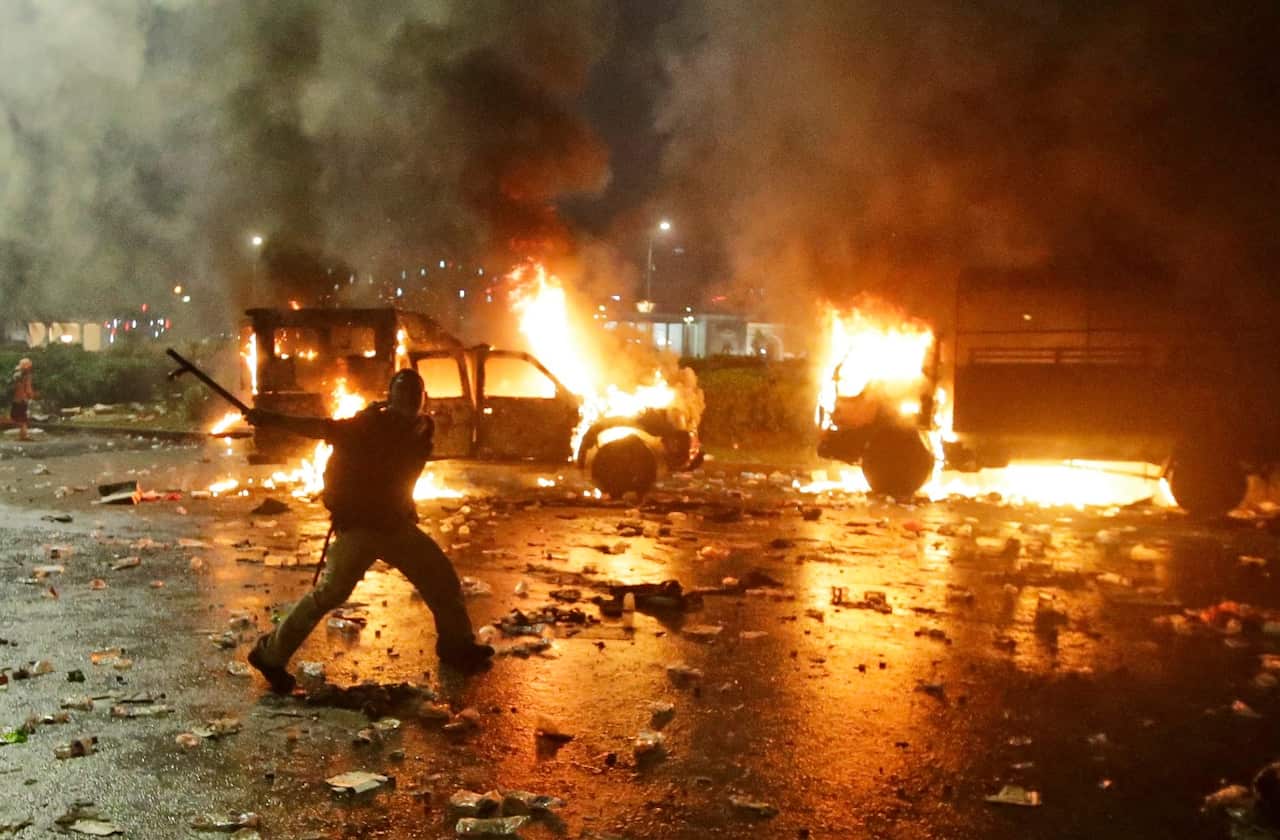 A protester waves a baton as police trucks are seen burning during a clash outside the presidential palace in Jakarta, Indonesia, Friday, Nov. 4, 2016. (AAP)