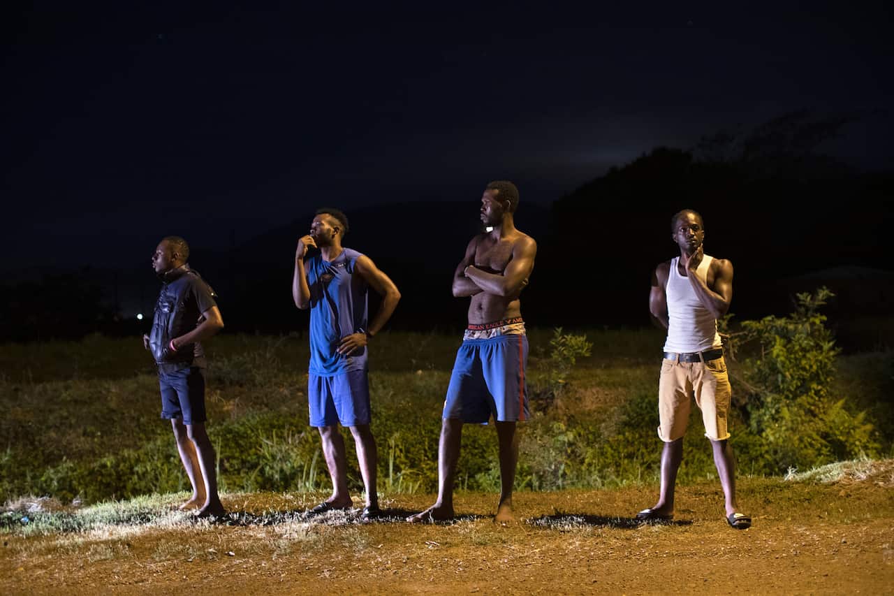 Residents look on as police investigate the scene of a shooting in Effortville, Jamaica