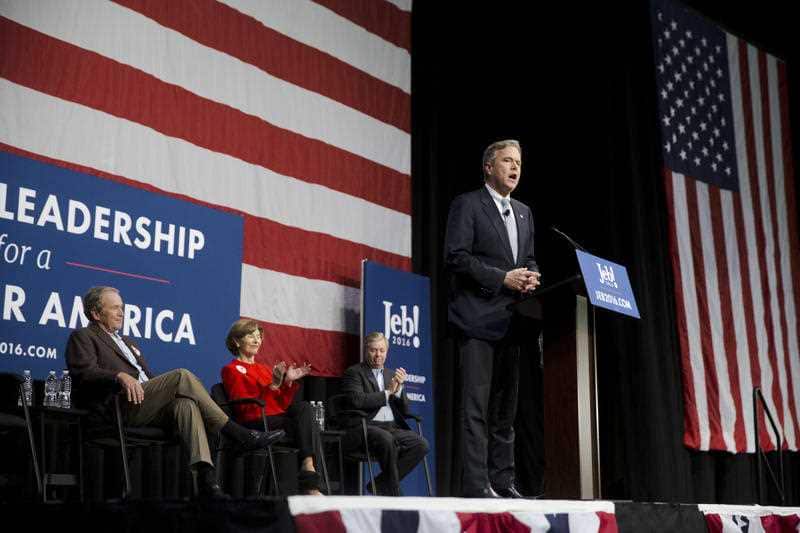 Former President George W. Bush listens to younger brother Jeb Bush give his speech to a packed auditorium of supporters.