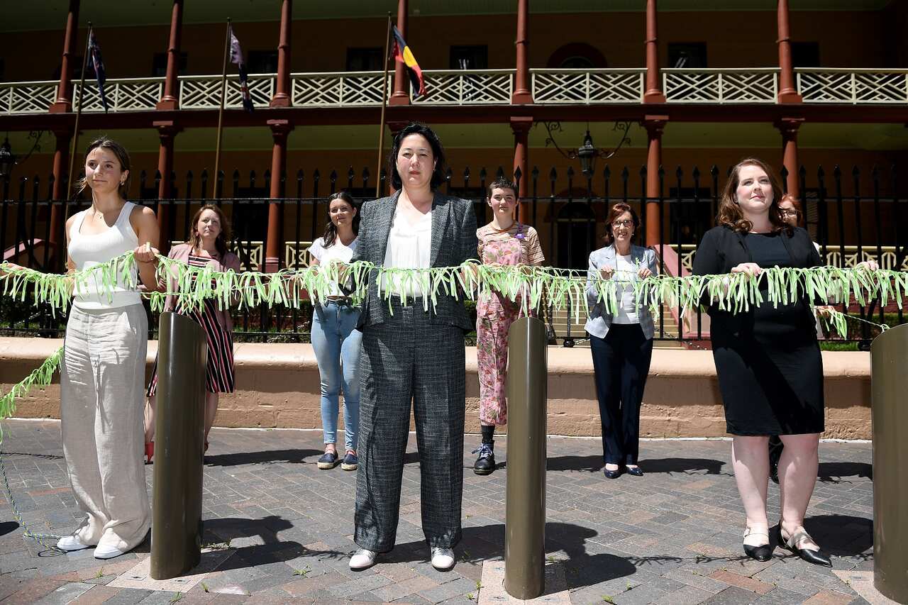 Greens MP Jenny Leong (centre) and others hang 6,000 green ribbons to each represent sexual assault complaints at NSW Parliament. 