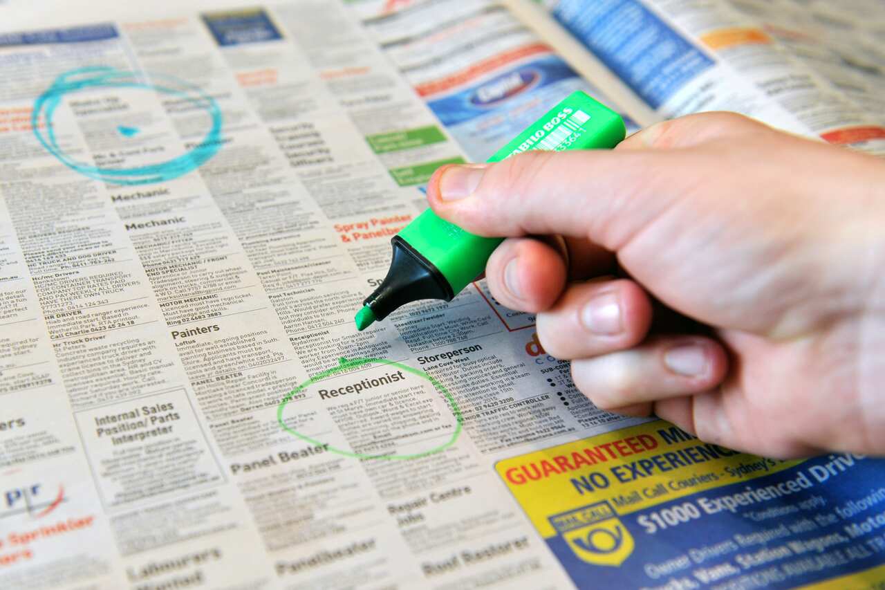 A hand circling a newspaper job advertisement with a green marker pen
