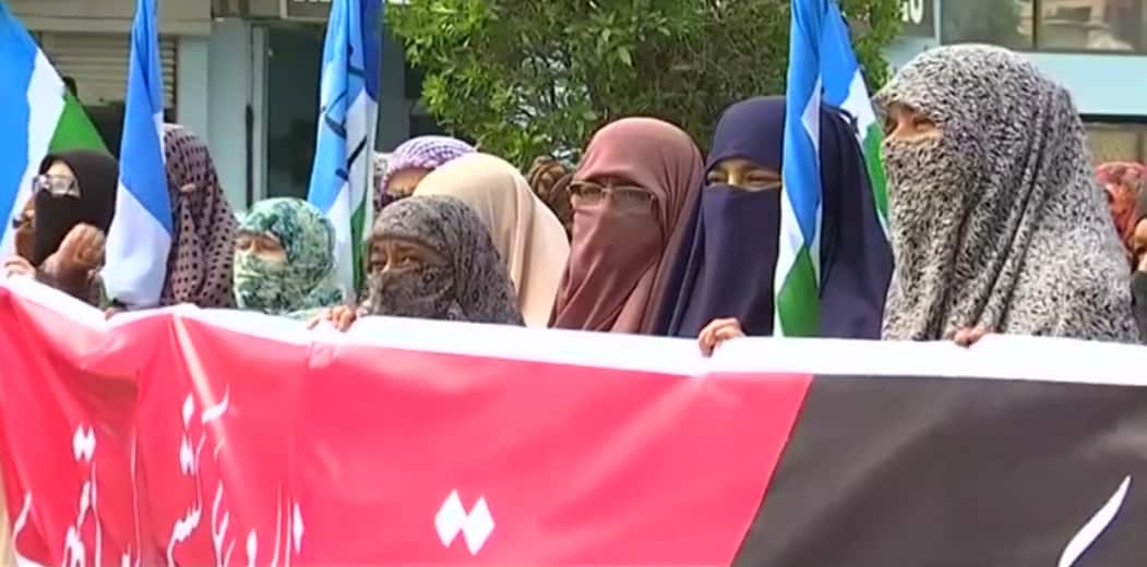 Groups of women hold banners in solidarity with the Kashmiri people.