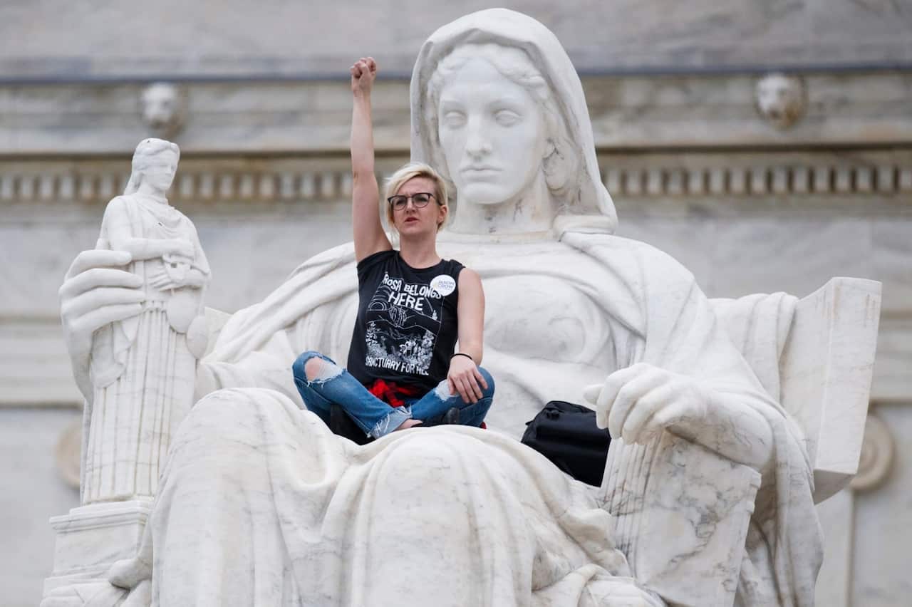 An activist protests the Senate confirmation of Supreme Court nominee Brett Kavanaugh from the lap of Contemplation of Justice at the Supreme Court 