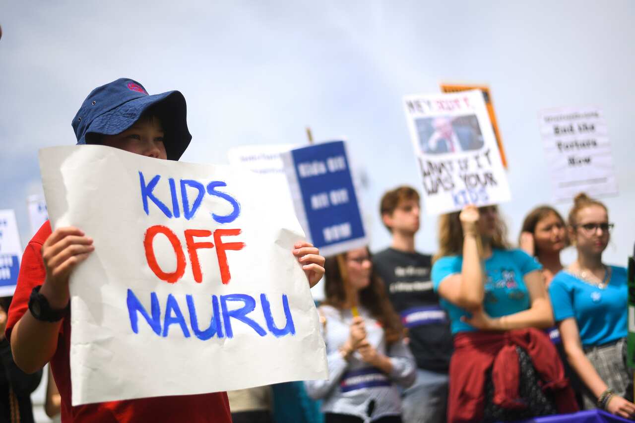 Protesters hold up signs during a rally demanding the resettlement of kids held on Nauru outside Parliament House in Canberra.