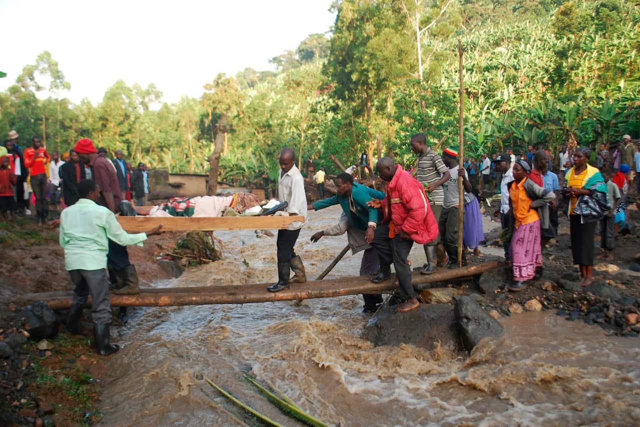 Residence carry an injured person over a river filled with mud in Bududa District, Uganda, Friday, Oct. 12, 2018. 
