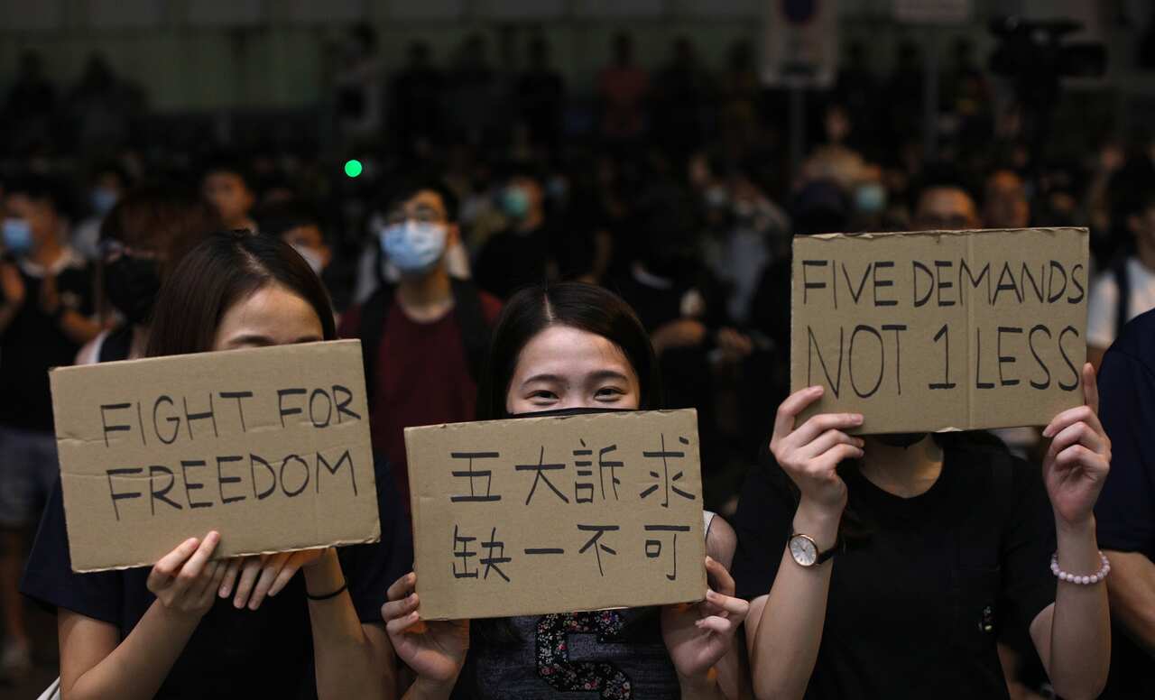 Anti government protesters hold up placards during a rally outside Queen Elizabeth stadium as Carrie Lam speaks. 