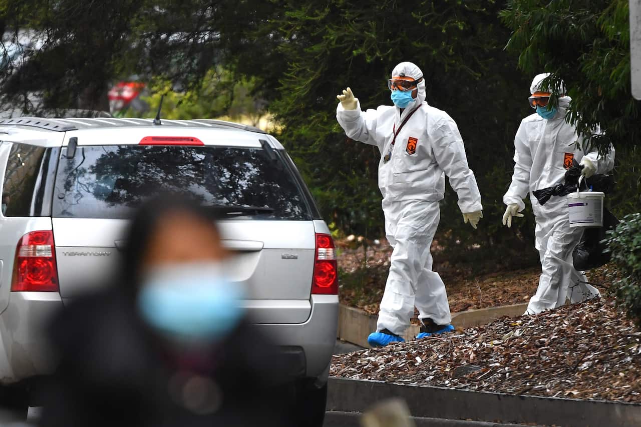 Workers in hazardous material overalls are seen outside of a public housing tower along Racecourse Road in Melbourne.