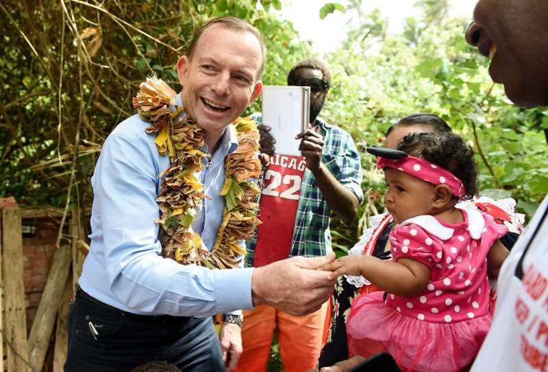 Prime minister Tony Abbott holds the hand of a child as he visits the grave of land rights activist Eddie Mabo on Mer Island.