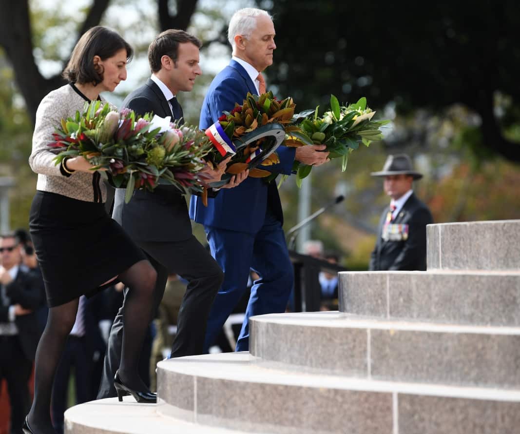 President of France Emmanuel Macron (centre) walks carrying a floral wreath tribute with NSW Premier Gladys Berejiklian (left) and Australian Prime Minister Malcolm Turnbull