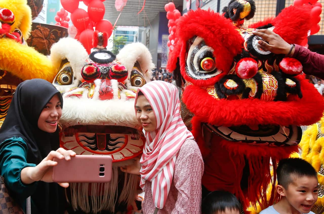 Muslims women take pictures with the lion dance at a shopping mall ahead of the Lunar New Year celebrations in Kuala Lumpur, Malaysia, Saturday, Feb. 10, 2018.