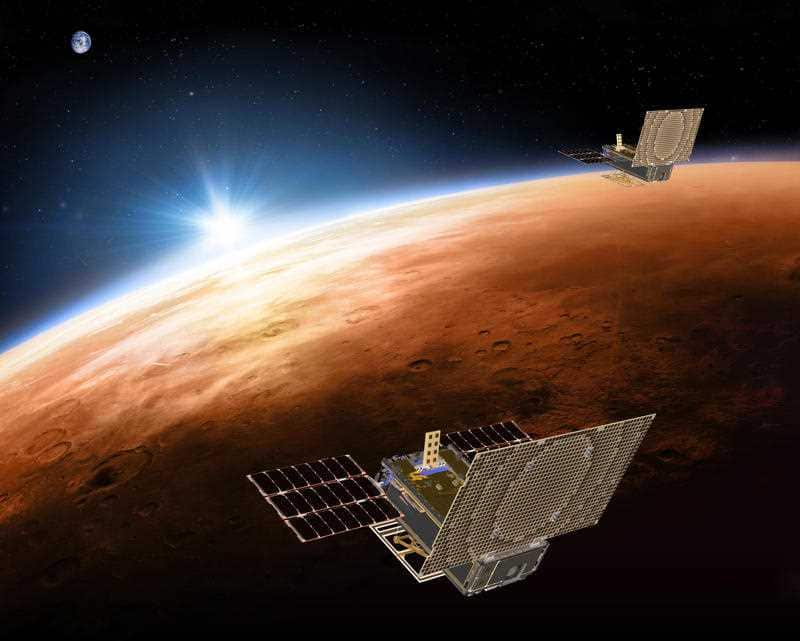 The the twin Mars Cube One project (MarCO) spacecrafts flying over Mars with Earth and the sun in the distance.