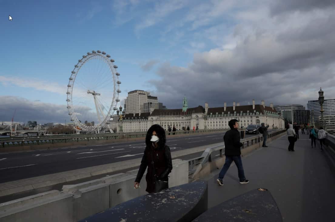 A woman wearing a face mask walks over a near empty Westminster Bridge backdropped by the London Eye ferris wheel in central London.