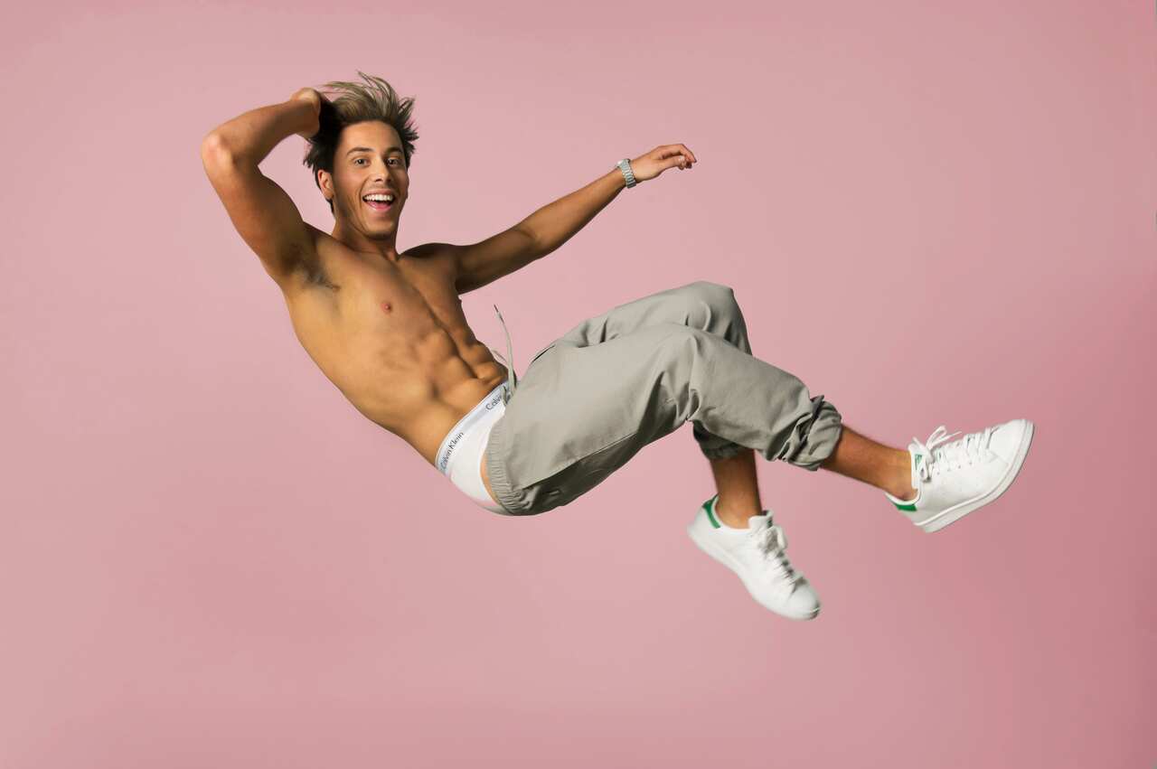 Max Key shirtless mid-air, smiling against a pink background