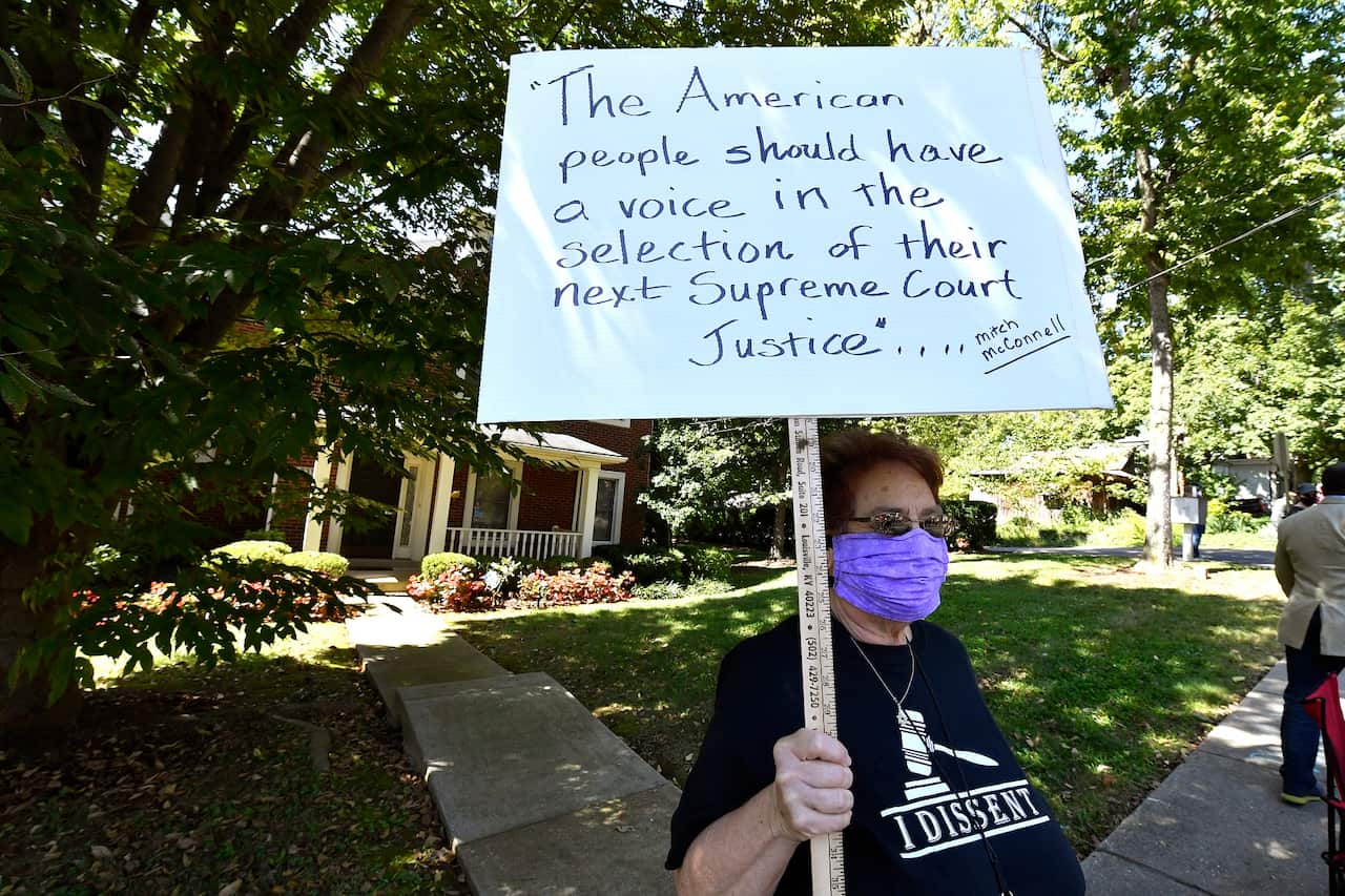 A protester stands outside the house of Senate Majority Leader Mitch McConnell.
