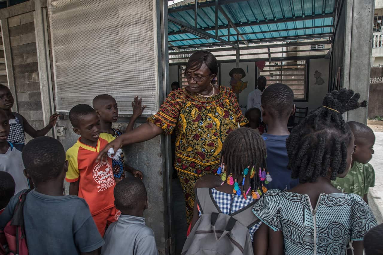 Pre-school principal Tirangue Doumbia ushers students into a new classroom built of recycled plastic bricks.