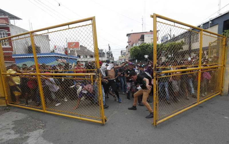 The migrant caravan bursts through the border gate.